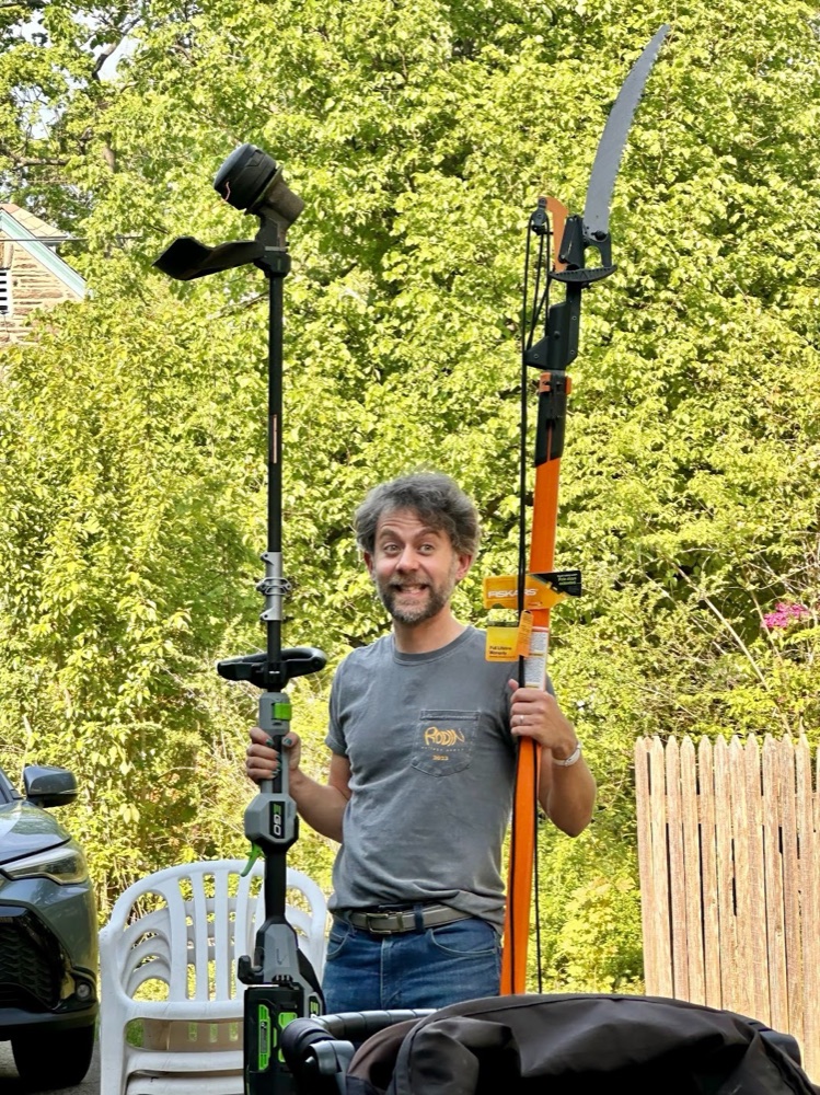 Jordan B. Warner grinning while holding a string trimmer and a pole saw